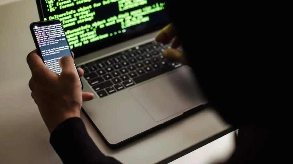 Person holding mobile phone in front of laptop